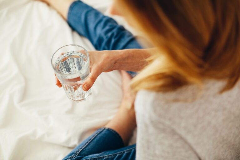 Woman sitting on a bed holding a cup of water