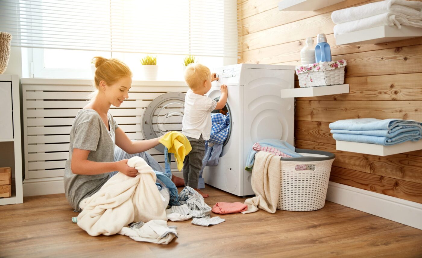 woman putting laundry into machine with child